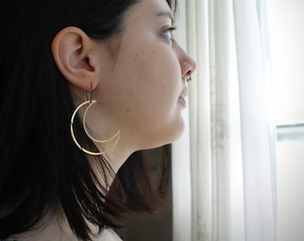May include: A person wearing a pair of gold crescent moon earrings. The earrings are hanging from their earlobes and are made of a thin metal.