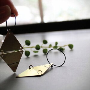 May include: A pair of gold triangle earrings with black wire hoops. The earrings are layered and have a geometric design.