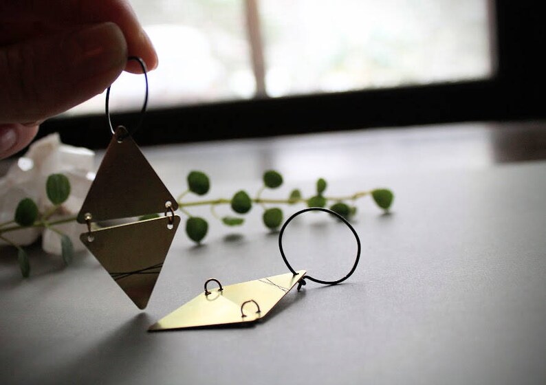 May include: A pair of gold triangle earrings with black wire hoops. The earrings are layered and have a geometric design.