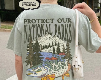 May include: A light green t-shirt with a graphic print of a fish and a mountain scene. The text "Protect Our National Parks" is printed on the shirt. The text "Explore Responsibly" is printed below the graphic.