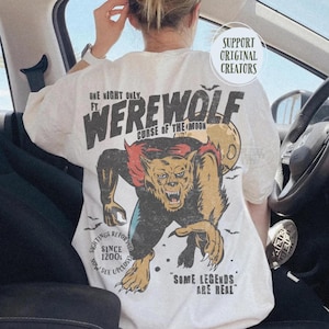 May include: An off-white t-shirt featuring a graphic of a snarling werewolf with red fur accents and a yellow moon. Text includes "ONE NIGHT ONLY FT. WEREWOLF CURSE OF THE MOON", "SIGHTINGS REPORTED SINCE 1200S", "NOW SEE UPCLOSE", and "SOME LEGENDS ARE REAL".