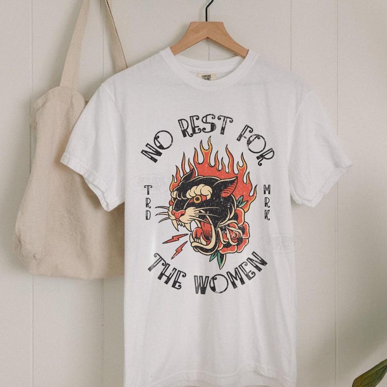 May include: White t-shirt with a vintage graphic. The design features a black panther with red flames, a red rose, and the text "NO REST FOR THE WOMEN". A beige tote bag hangs on the left.