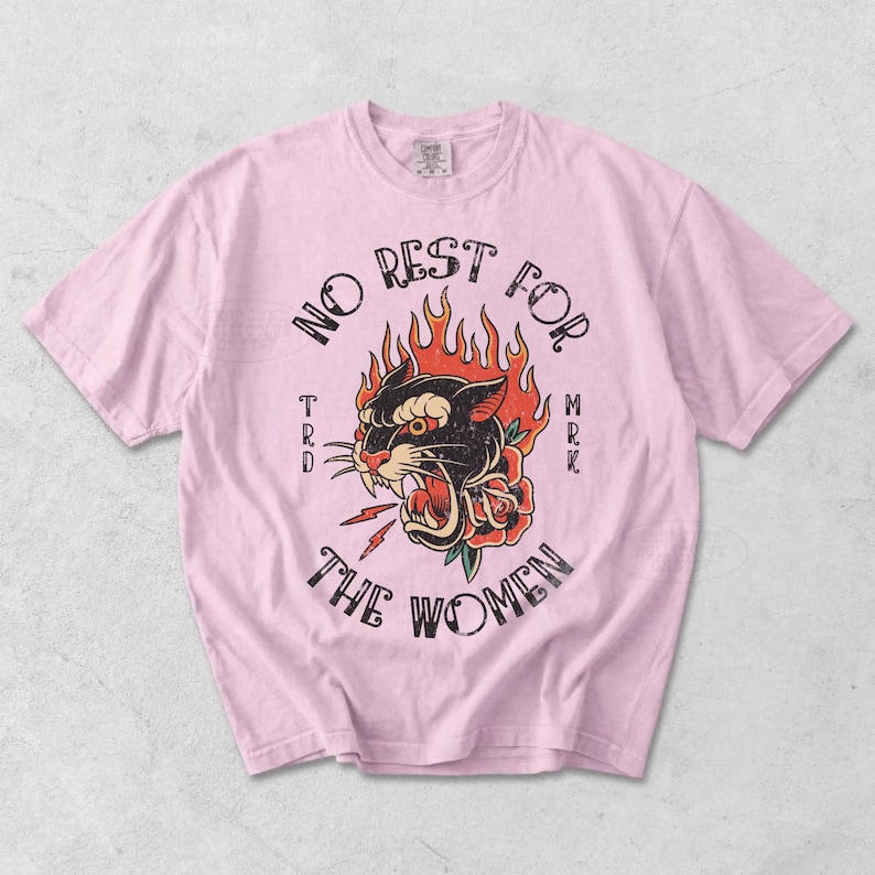 May include: Pale pink t-shirt with a vintage tattoo-style design. The design features a black panther with flames, a rose, and the words "NO REST FOR THE WOMEN".