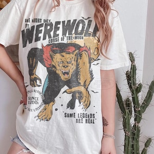 May include: An off-white short-sleeve t-shirt featuring a graphic of a werewolf with the text "ONE NIGHT ONLY FT. WEREWOLF CURSE OF THE MOON", "SIGHTINGS REPORTED SINCE 1200s", "NOW SEE UPCLOSE", and "SOME LEGENDS ARE REAL" in a distressed black font.