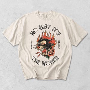 May include: Off-white t-shirt with a black panther graphic surrounded by flames and a rose, and the words "NO REST FOR THE WOMEN." The design is in a vintage tattoo style.