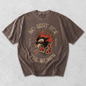 May include: Brown t-shirt featuring a black panther design with red flames and a rose. The text "NO REST FOR THE WOMEN" is arched above the panther. The shirt has a vintage, worn appearance.