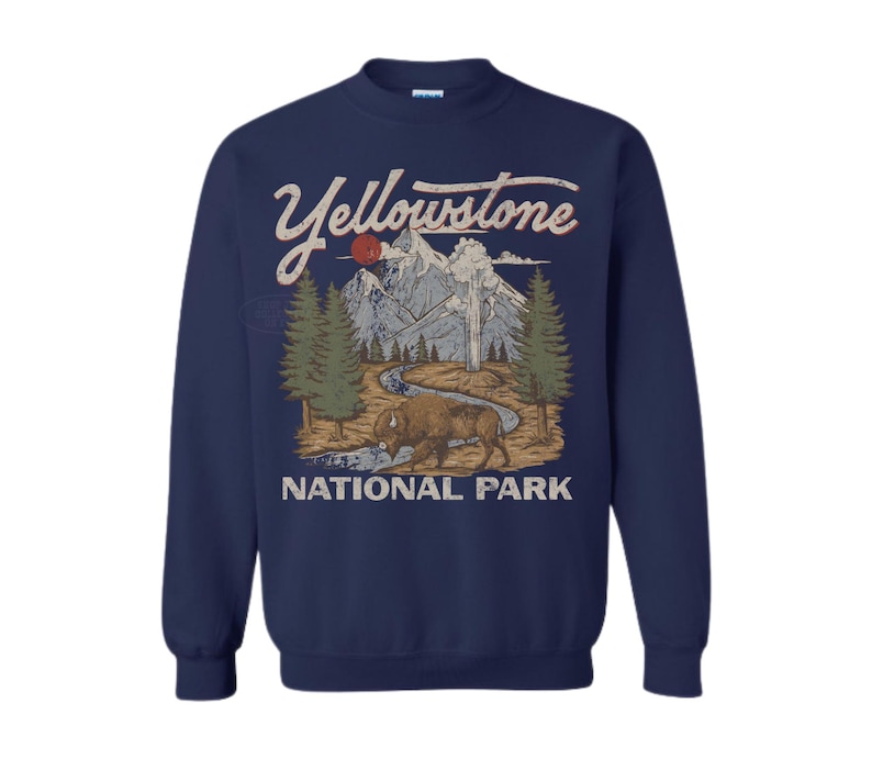 May include: A navy blue crewneck sweatshirt featuring a graphic print of Yellowstone National Park. The design includes a brown bison, a winding river, green pine trees, and grey mountains under a red sun, with the text Yellowstone National Park.