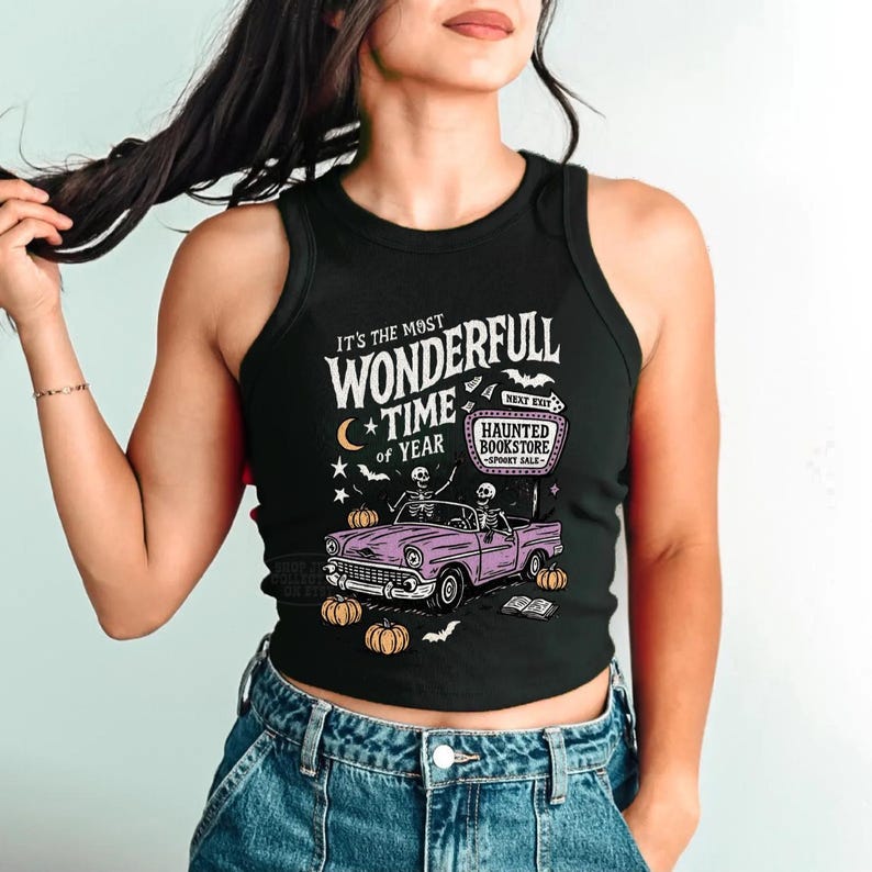 May include: Black tank top with a Halloween-themed graphic. The design features the text "It's the Most Wonderfull Time of Year" with a vintage car carrying skeletons, pumpkins, and the words "Haunted Bookstore".