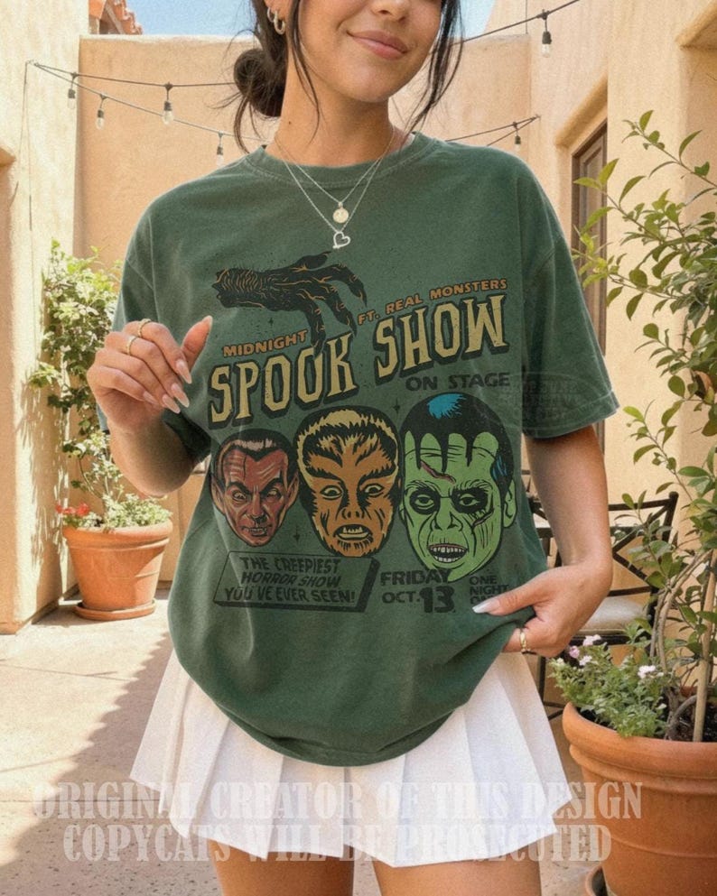 May include: A forest green short-sleeve t-shirt featuring a graphic print with the text Midnight Spook Show, Ft. Real Monsters, On Stage, The Creepiest Horror Show You've Ever Seen, and Friday Oct. 13, along with illustrations of three monster faces.