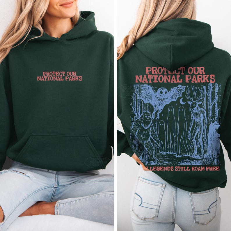 May include: A dark green hooded sweatshirt featuring the text "PROTECT OUR NATIONAL PARKS" in red on the front. The back displays a blue graphic of a forest scene with a large creature, an owl, and ghost-like figures with the text "LEGENDS STILL ROAM FREE."