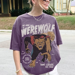 May include: A purple short-sleeve t-shirt featuring a graphic of a werewolf with the text "ONE NIGHT ONLY FT. WEREWOLF CURSE OF THE MOON", "SIGHTINGS REPORTED SINCE 1200s NOW SEE UPCLOSE", and "SOME LEGENDS ARE REAL" printed in white and tan.