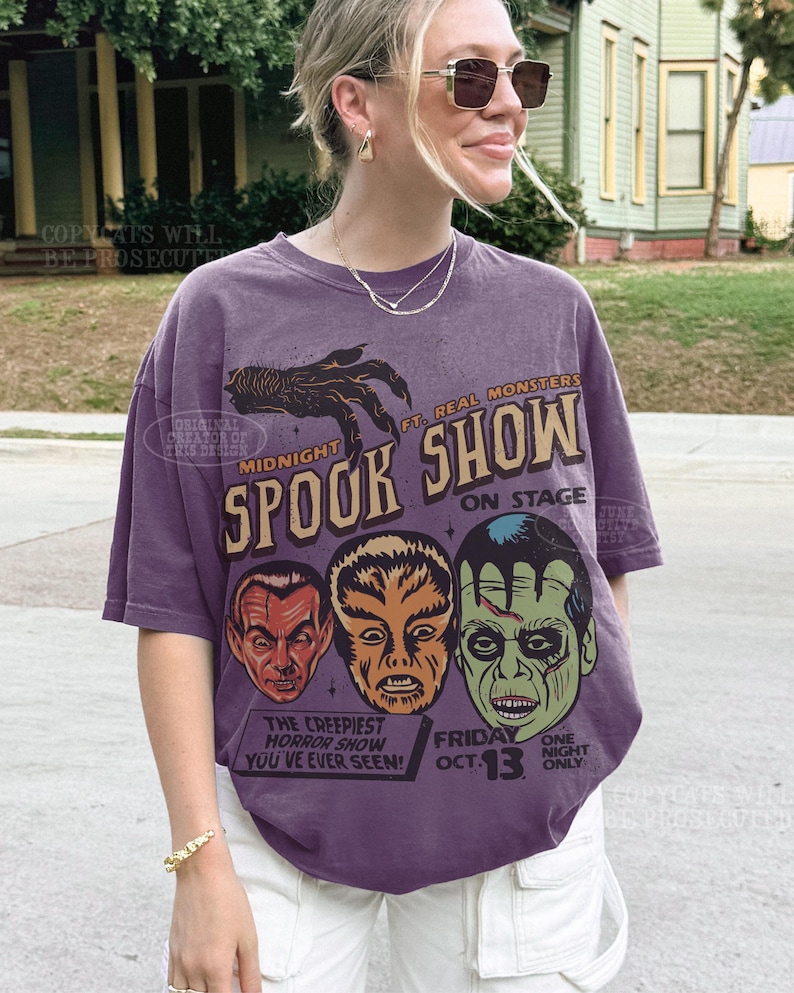 May include: A purple short-sleeve t-shirt featuring a graphic print with the text Midnight Spook Show, Ft. Real Monsters, On Stage, The Creepiest Horror Show You've Ever Seen, Friday Oct. 13, and One Night Only, alongside illustrations of three monster faces.