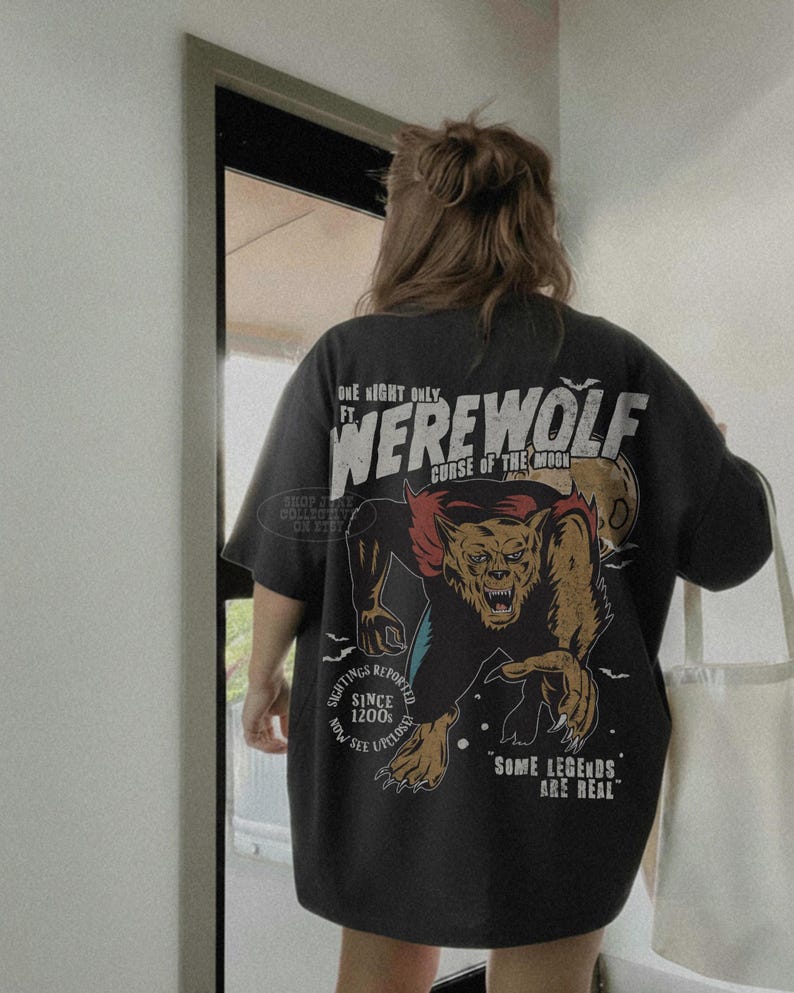 May include: A charcoal gray t-shirt featuring a large graphic on the back. The design depicts a werewolf with the text "ONE NIGHT ONLY FT. WEREWOLF CURSE OF THE MOON," "SIGHTINGS REPORTED SINCE 1200s," and "SOME LEGENDS ARE REAL" in white and red.
