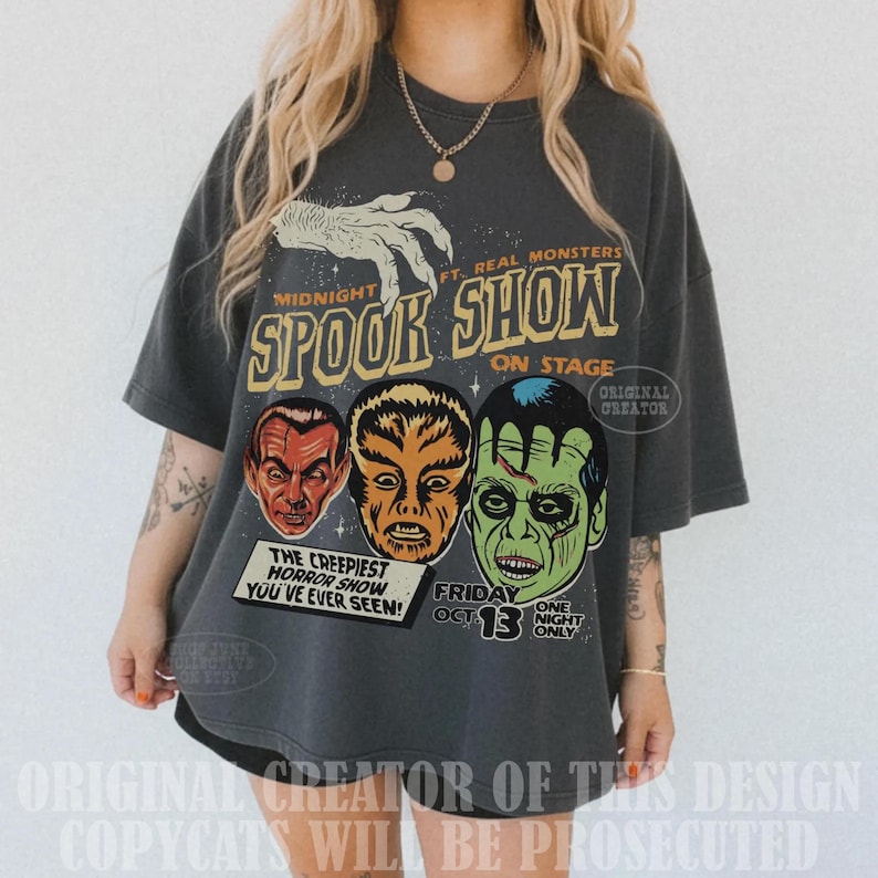 May include: A charcoal gray oversized t-shirt featuring a graphic print with the text Midnight Spook Show On Stage. The design includes a white hand illustration and three monster faces in red, orange, and green, with the text The Creepiest Horror Show You've Ever Seen and Friday Oct 13 One Night Only.