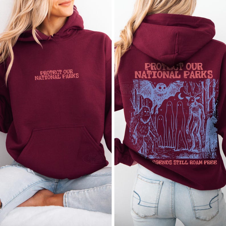 May include: A maroon hooded sweatshirt featuring the text "PROTECT OUR NATIONAL PARKS" on the front. The back displays a blue graphic illustration of a forest with a bat, a sasquatch, ghosts, and a deer, with the text "PROTECT OUR NATIONAL PARKS" and "LEGENDS STILL ROAM FREE."