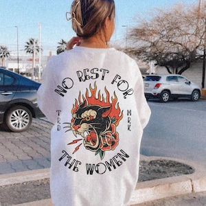 May include: White sweatshirt with a graphic design on the back. The design features a black panther with red flames, a red rose, and the text "NO REST FOR THE WOMEN". The sweatshirt is a casual style.
