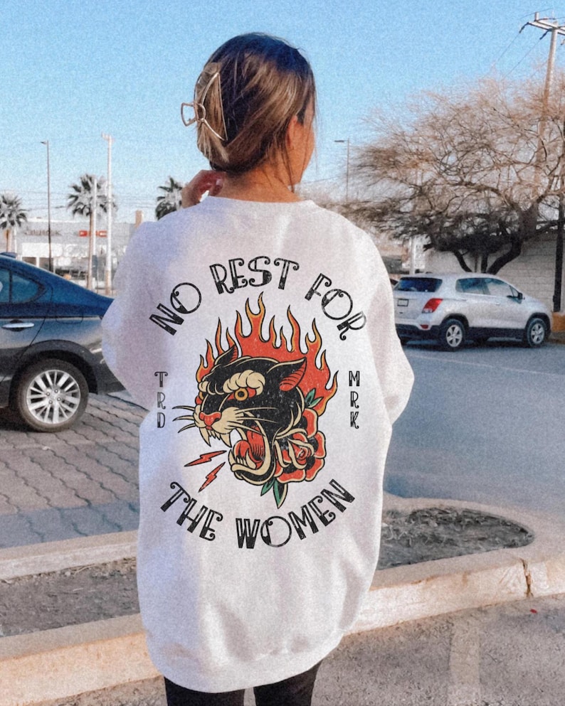 May include: White sweatshirt with a graphic design on the back. The design features a black panther with red flames, a red rose, and the text "NO REST FOR THE WOMEN". The sweatshirt is a casual style.