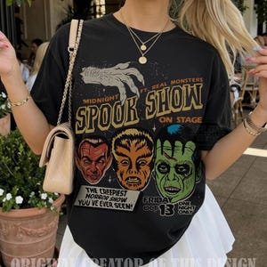 May include: A black t-shirt featuring a graphic print with the text Midnight Spook Show, Ft. Real Monsters, On Stage, The Creepiest Horror Show You've Ever Seen, Friday Oct 13, One Night Only. The design includes a claw and three monster faces.
