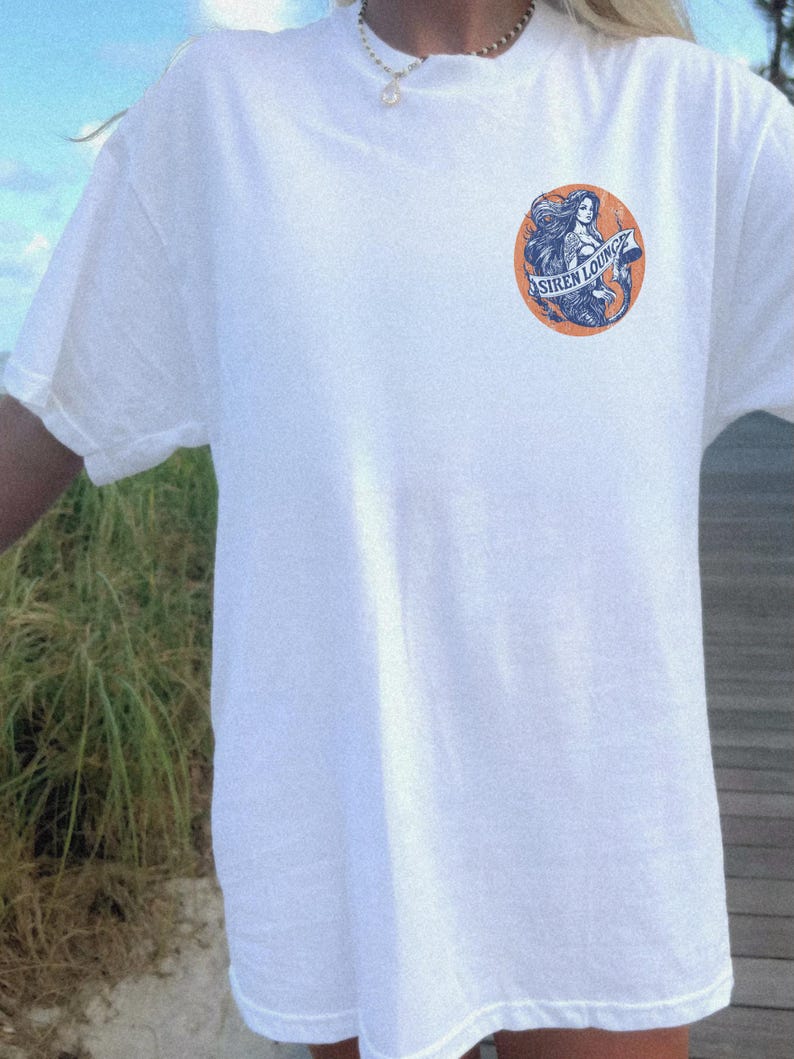 May include: White t-shirt with a graphic of a mermaid with the text "Siren Lounge" on a circular orange background.