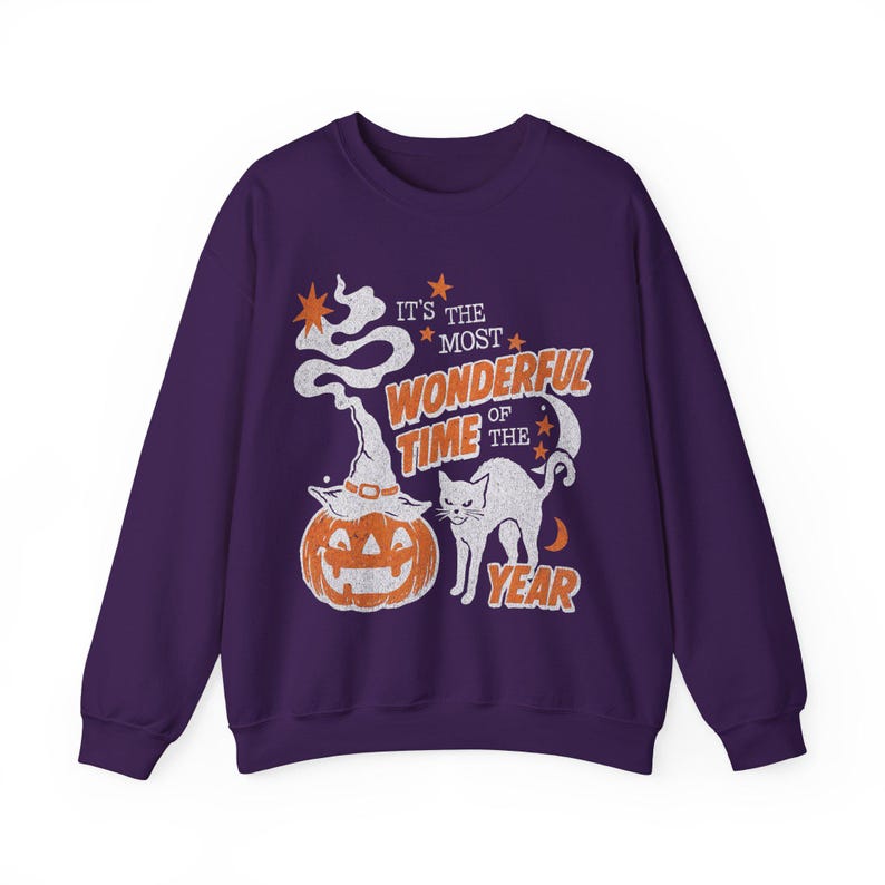 Peut inclure: Un sweat-shirt &agrave; manches longues violet fonc&eacute; avec une impression graphique repr&eacute;sentant une citrouille d'Halloween avec un chapeau de sorci&egrave;re, un chat noir et le texte "IT'S THE MOST WONDERFUL TIME OF THE YEAR" en orange et blanc.