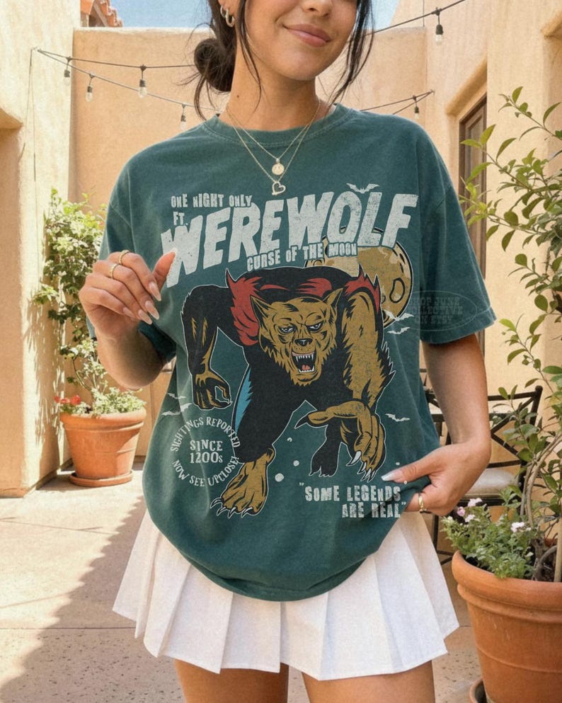 May include: A dark green t-shirt featuring a graphic of a werewolf with the text "ONE NIGHT ONLY FT. WEREWOLF CURSE OF THE MOON", "SIGHTINGS REPORTED SINCE 1200S NOW SEE UPCLOSE", and "SOME LEGENDS ARE REAL" paired with a white pleated mini skirt.