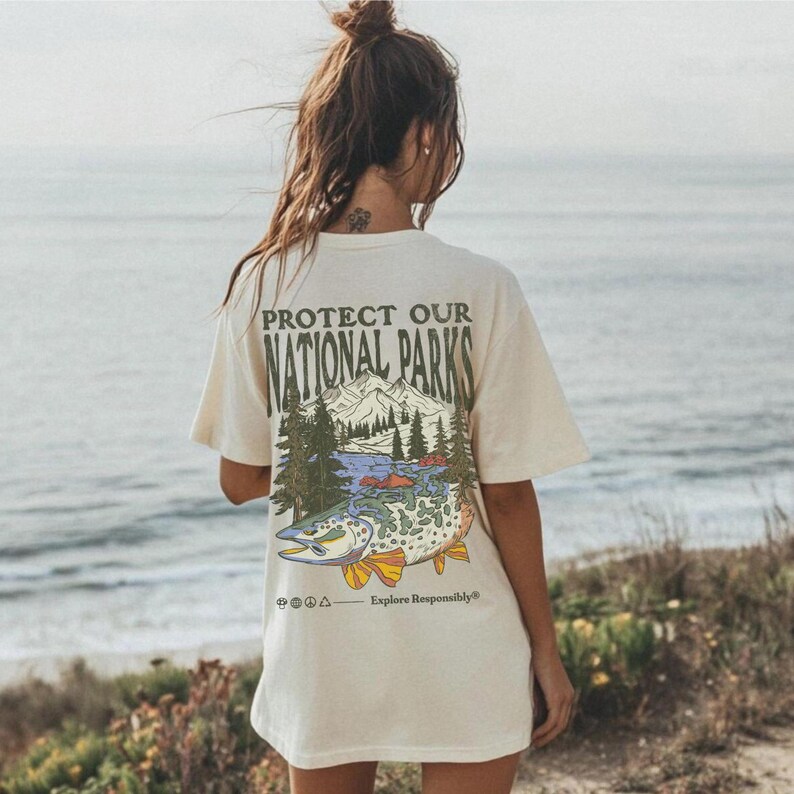 May include: A white t-shirt with a graphic print of a mountain scene and a fish. The text "Protect Our National Parks" is printed on the shirt. The text "Explore Responsibly" is printed below the graphic.