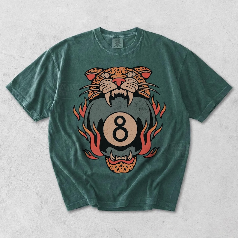 May include: Green t-shirt featuring a graphic of a tiger's head above a flaming eight ball. The tiger design is in shades of orange, brown, and black. The number eight is in a circle. The shirt is a casual wear item.