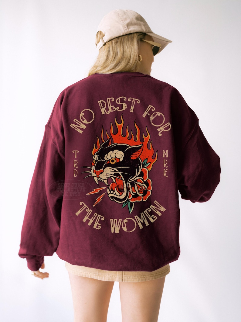 May include: Burgundy sweatshirt with a graphic on the back featuring a black panther with red flames, a rose, and the text "NO REST FOR THE WOMEN". The sweatshirt has long sleeves and a relaxed fit.