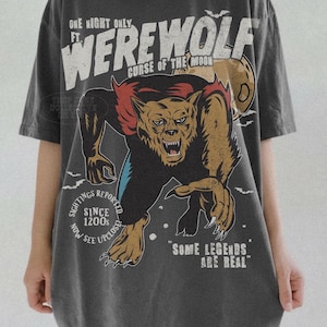 May include: A charcoal gray short-sleeve t-shirt featuring a graphic of a snarling werewolf. The text reads: ONE NIGHT ONLY FT. WEREWOLF CURSE OF THE MOON, SIGHTINGS REPORTED SINCE 1200S NOW SEE UPCLOSE, and SOME LEGENDS ARE REAL, with small bats.