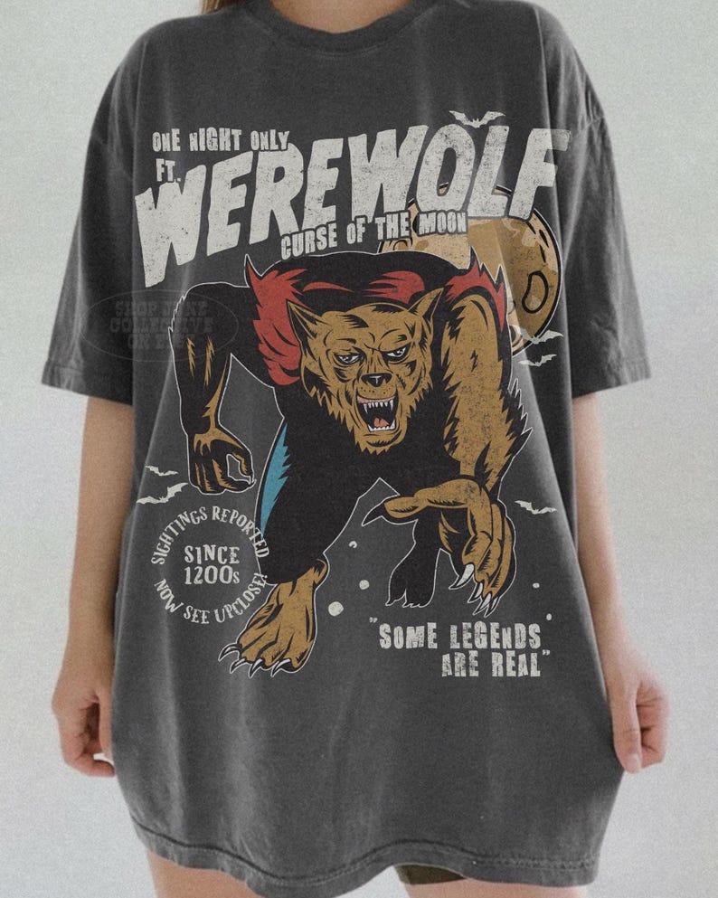 May include: A charcoal gray short-sleeve t-shirt featuring a graphic of a snarling werewolf. The text reads: ONE NIGHT ONLY FT. WEREWOLF CURSE OF THE MOON, SIGHTINGS REPORTED SINCE 1200S NOW SEE UPCLOSE, and SOME LEGENDS ARE REAL, with small bats.