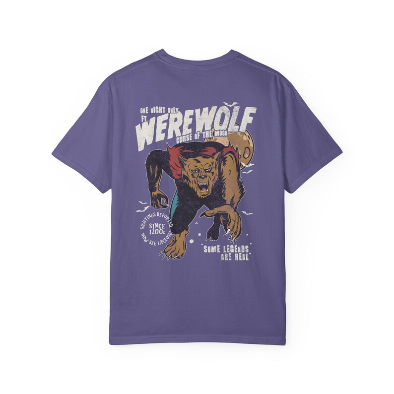 May include: A purple short-sleeve t-shirt featuring a graphic of a brown werewolf with red fur accents. The text reads: ONE NIGHT ONLY FT. WEREWOLF CURSE OF THE MOON, SIGHTINGS REPORTED SINCE 1200S, NOW SEE UPLOAD, SOME LEGENDS ARE REAL.