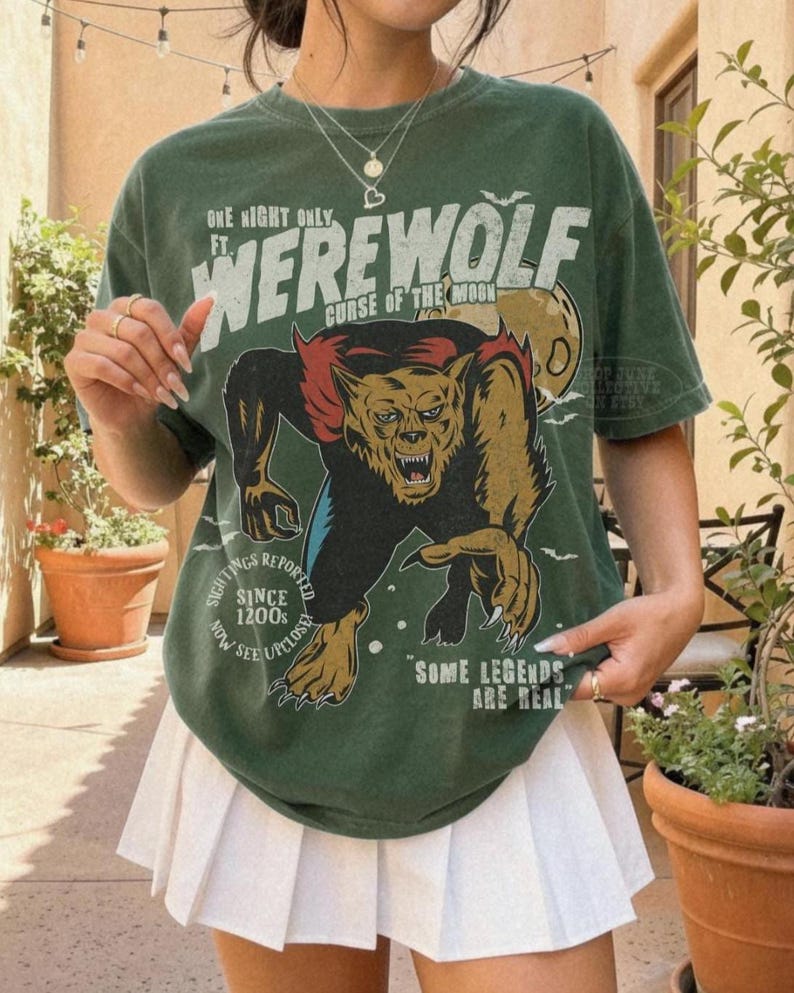 May include: A forest green short-sleeve t-shirt featuring a graphic of a werewolf with the text "ONE NIGHT ONLY FT. WEREWOLF CURSE OF THE MOON SIGHTINGS REPORTED SINCE 1200S NOW SEE UPCLOSE SOME LEGENDS ARE REAL" in white and yellow lettering.