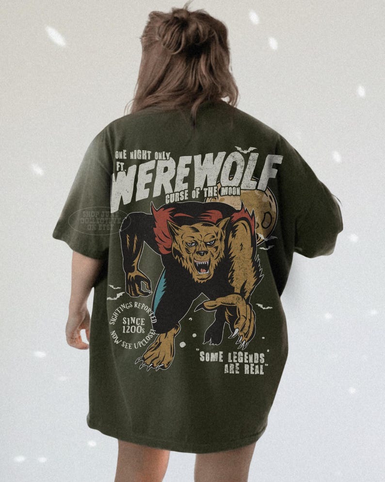 May include: An olive green t-shirt featuring a large graphic on the back of a snarling werewolf with red fur accents and a full moon. The text reads: ONE NIGHT ONLY FT. WEREWOLF CURSE OF THE MOON, SIGHTINGS REPORTED SINCE 1200S NOW SEE UPCLOSE, SOME LEGENDS ARE REAL.