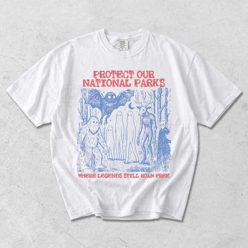 Peut inclure: Un t-shirt blanc &agrave; manches courtes avec une impression graphique bleue repr&eacute;sentant une for&ecirc;t peupl&eacute;e d'un papillon de nuit, d'un sasquatch, de fant&ocirc;mes, d'une cr&eacute;ature &agrave; bois et d'un alien. Le texte rouge indique PROTECT OUR NATIONAL PARKS.