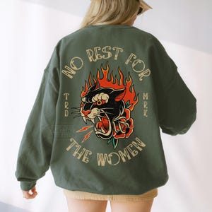 May include: Green sweatshirt with a graphic of a black panther with red flames and a rose. The text "NO REST FOR THE WOMEN" is arched above the panther. The sweatshirt is a solid green color.