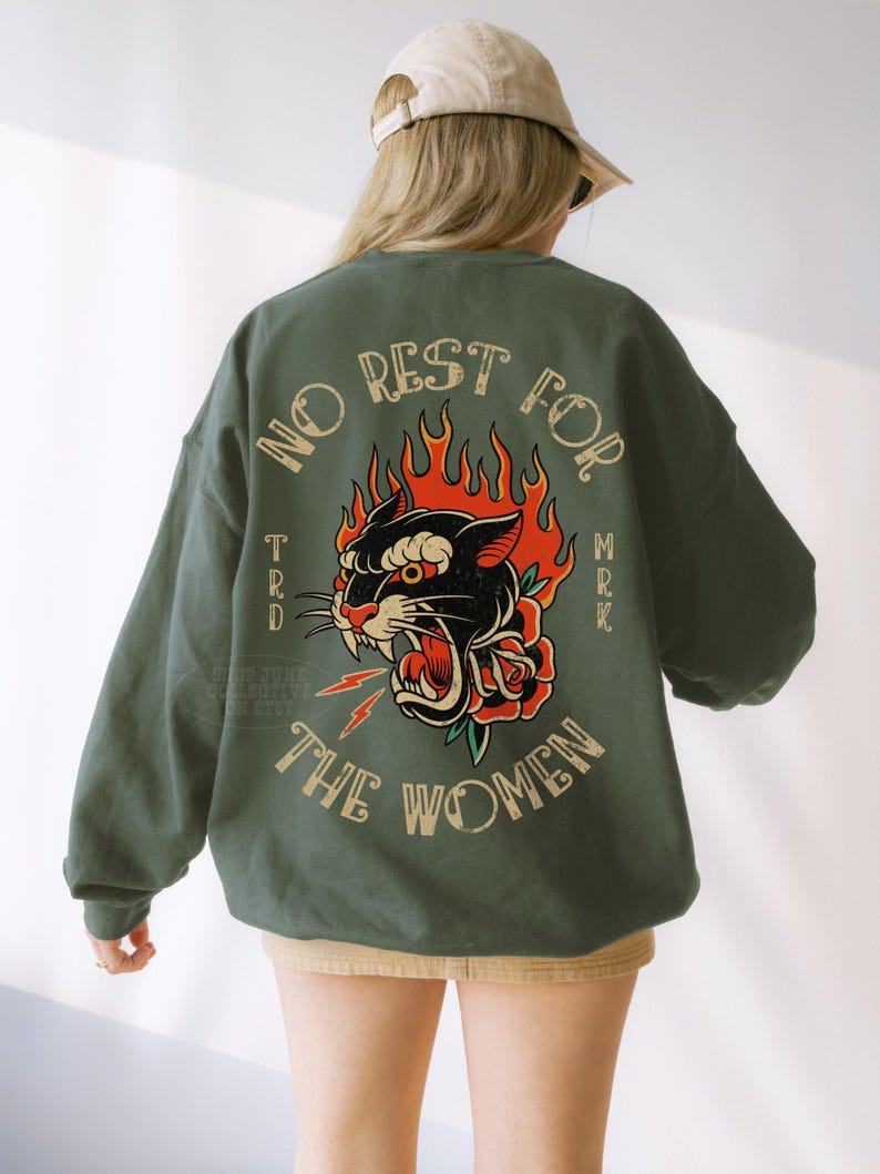 May include: Green sweatshirt with a graphic of a black panther with red flames and a rose. The text "NO REST FOR THE WOMEN" is arched above the panther. The sweatshirt is a solid green color.