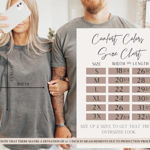 Pode incluir: Duas pessoas vestindo camisetas cinza Comfort Colors. Uma tabela de tamanhos mostra medidas em polegadas para v&aacute;rios tamanhos, de S a 3XL. A tabela inclui dimens&otilde;es de largura e comprimento para cada tamanho, com uma nota sobre poss&iacute;veis desvios.