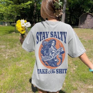 May include: Gray t-shirt with a graphic of a mermaid with the text "Stay Salty Siren Lounge Take No Shit" printed on the back.