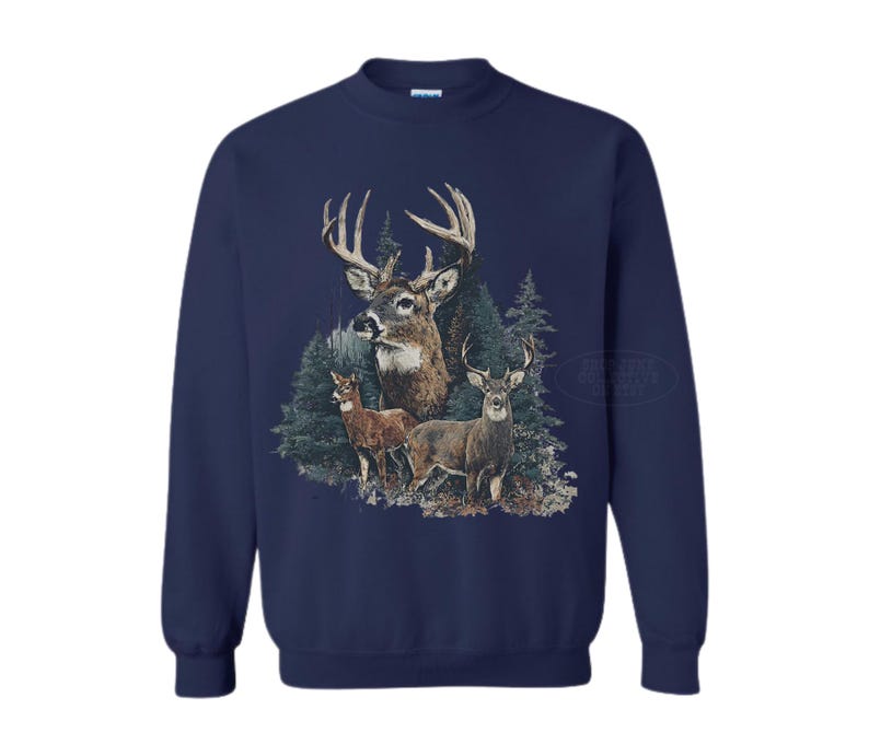 Puede incluir: Sudadera azul marino con un gr&aacute;fico detallado de ciervos en un entorno forestal. El dise&ntilde;o incluye tres ciervos, con un gran macho prominentemente exhibido, y &aacute;rboles de hoja perenne en el fondo. La sudadera tiene mangas largas y cuello redondo.