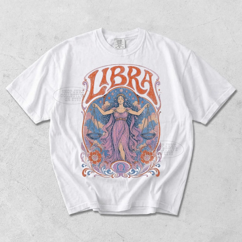 May include: A white short-sleeve t-shirt featuring a large graphic print on the chest. The design displays the word LIBRA in orange letters above an illustration of a figure in a purple dress holding scales, surrounded by clouds, stars, and flowers.
