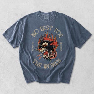 May include: A blue short-sleeved t-shirt with a faded appearance. The front displays a graphic of a black panther with flames, a rose, and the text "NO REST FOR THE WOMEN".