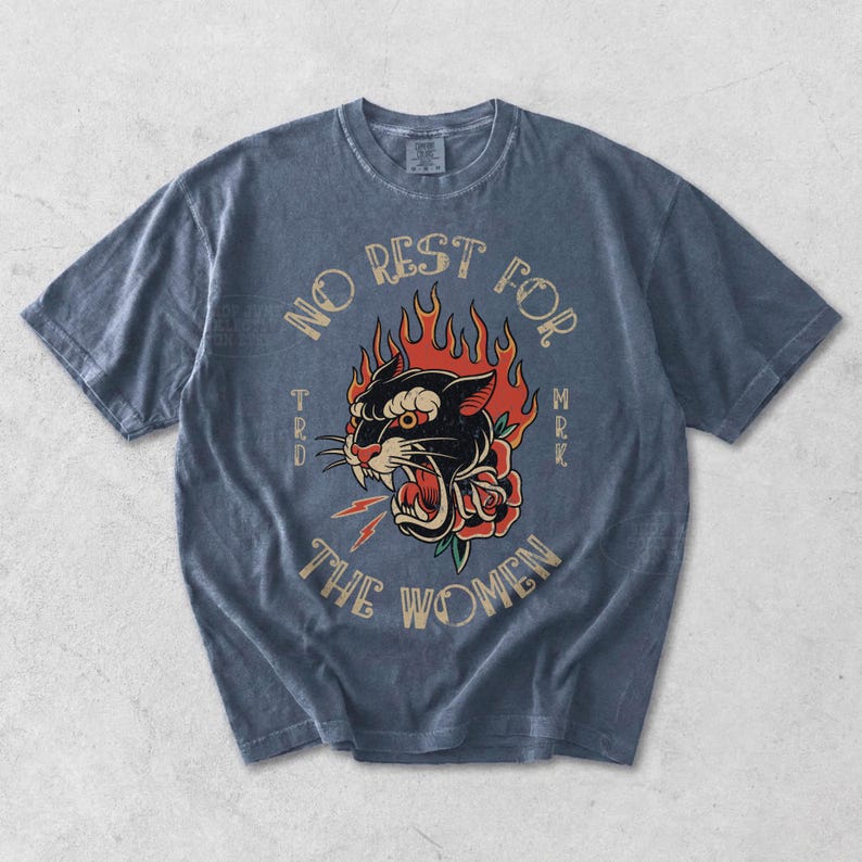 May include: A blue short-sleeved t-shirt with a faded appearance. The front displays a graphic of a black panther with flames, a rose, and the text "NO REST FOR THE WOMEN".
