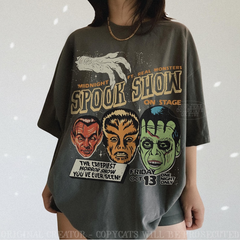 May include: A charcoal gray short-sleeve t-shirt featuring a graphic print with the text MIDNIGHT SPOOK SHOW FT. REAL MONSTERS ON STAGE. The design includes a white clawed hand, three monster faces, and the text THE CREEPIEST HORROR SHOW YOU'VE EVER SEEN!