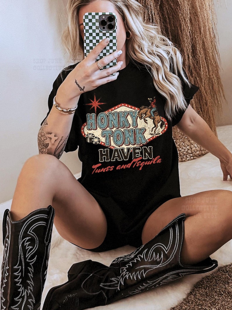 Pode incluir: Camiseta preta com a frase "Honky Tonk Haven Tunes and Tequila" em um design retr&ocirc;. A imagem tamb&eacute;m mostra botas de cowboy pretas com costuras brancas.