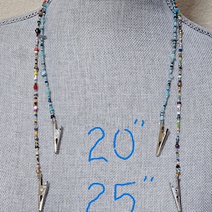 May include: A beaded lanyard featuring a variety of small, multi-colored glass beads in shades of blue, red, yellow, and clear. The lanyard includes two silver-toned metal clips at the ends. The text 20" and 25" is visible, indicating two lengths.