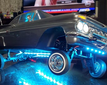 May include: A gray and silver model car with blue LED lights underneath. The car is a 1950s-style sedan with a chrome bumper and whitewall tires.