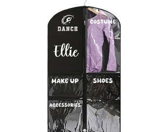 Könnte beinhalten: Schwarze Kleiderschutzhülle mit transparenten Fächern für Kostüm, Schuhe, Make-up und Accessoires. Die Tasche trägt den Namen "Ellie" in weißer Schrift und das Wort "DANCE" darüber. Ein lila Outfit hängt im Kostümfach.