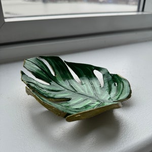 May include: A green and gold leaf-shaped dish with a textured surface. The dish is made of ceramic and has a realistic leaf design.