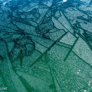 May include: Abstract pattern of teal and blue ice with a textured surface. The ice has a delicate, intricate pattern of lines and shapes.