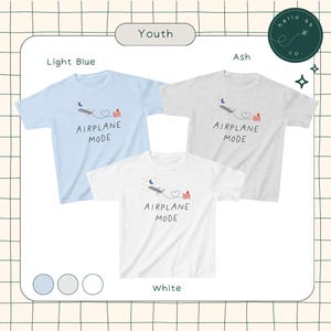 May include: Three youth t-shirts in light blue, ash grey, and white with a graphic of a plane flying over a heart and a building with the text "Airplane Mode".